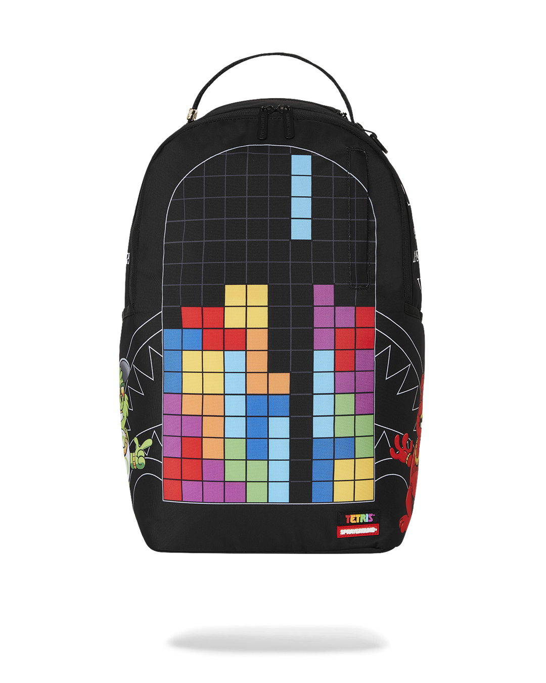 A black Sprayground backpack featuring a large, colorful design of a Tetris game in progress. The main panel shows a grid filled with various colored Tetris blocks. A green dragon is on the left side and a red monster is on the right. The bottom of the backpack has a tag that says "TETRIS" and "SPRAYGROUND."