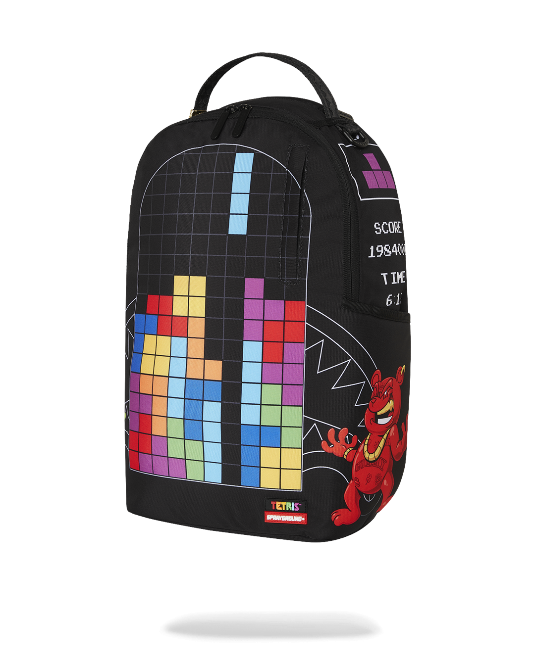 A black Sprayground backpack featuring a large, colorful design of a Tetris game in progress. A red monster with horns and a gold chain is on the right side of the main grid. A white graphic on the side of the bag reads "SCORE 1984066" and "TIME 6:14." A tag at the bottom of the main panel reads "TETRIS" and "SPRAYGROUND."
