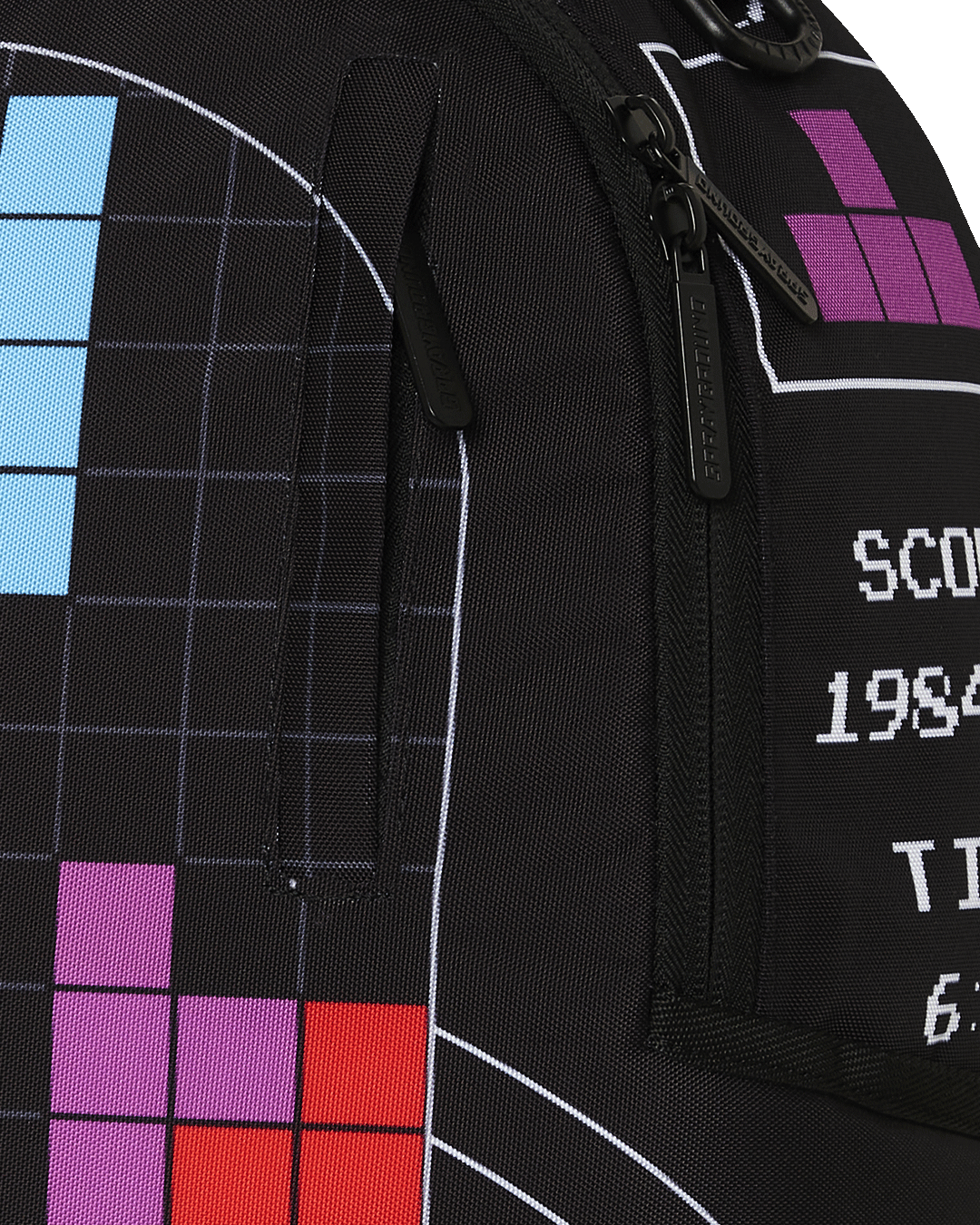 A close-up of a black Sprayground backpack featuring a Tetris design. The image focuses on the right side of the bag, showing a portion of the main Tetris game grid with colorful blocks, including red, purple, and blue. A black zipper with a silver pull is visible on the side, next to a white graphic that displays "SCORE 1984066" and "TIME 6:14." A small purple Tetris block is shown in a box above the score.