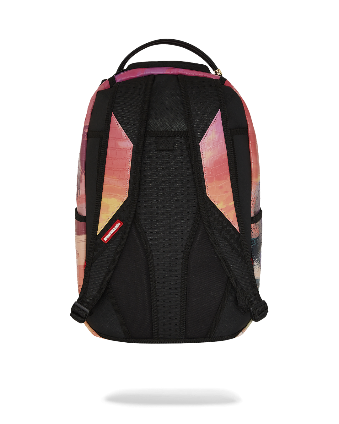 A back view of a colorful Sprayground backpack. The main straps are black and padded, with a sunset-colored graphic on the top portion that has a crocodile-skin texture. The back panel is black with a textured, padded finish for comfort. The top of the bag has a black handle. A red tag with the Sprayground logo is visible on the left strap.