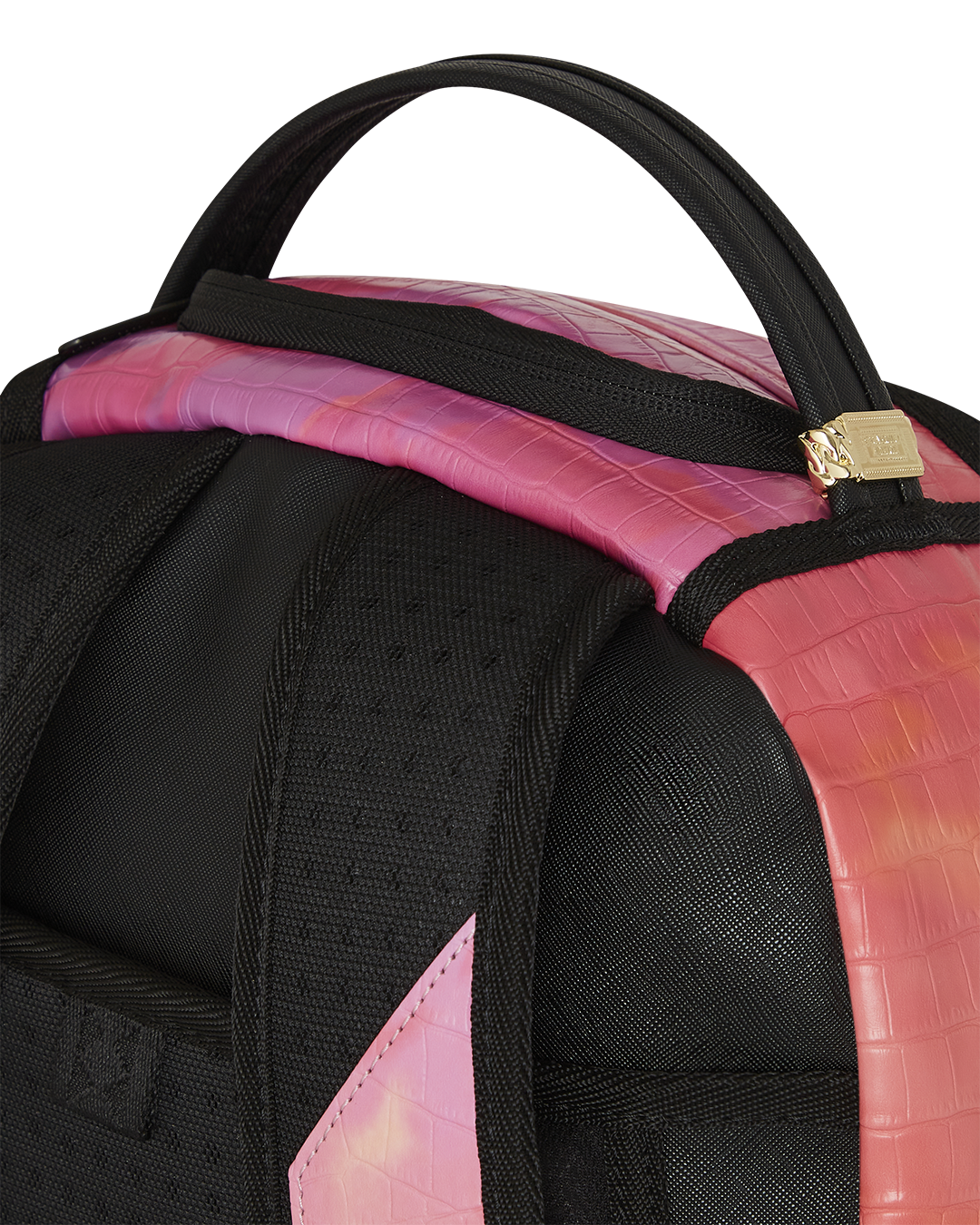 A close-up of the top of a black Sprayground backpack. The image shows the padded black handle and the top of the bag, which has a vibrant pink and orange sunset design with a subtle crocodile-skin texture. A small gold-toned metal tag is attached to the base of the handle. The black shoulder straps and padded back panel are also visible.
