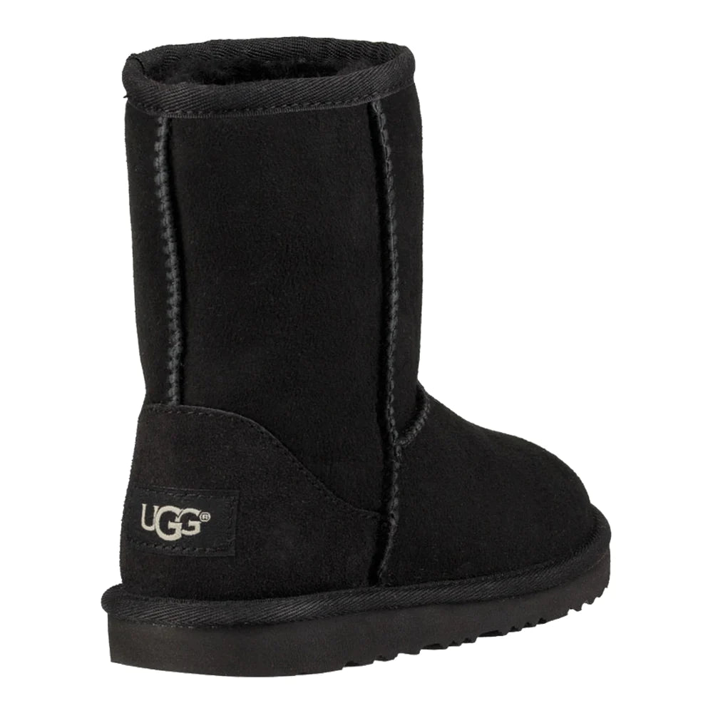 Rear view of a single UGG Kid’s Classic II boot in black suede. The image highlights the light gray UGG logo patch on the heel and the black wool lining visible at the cuff of the mid-calf shaft.