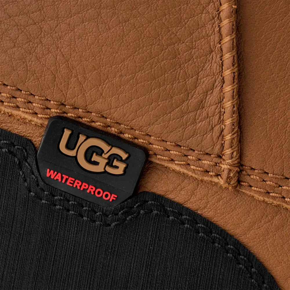 Close-up of the waterproof UGG logo badge on the Chestnut leather boot, showing the contrasting black textile and stitching detail.