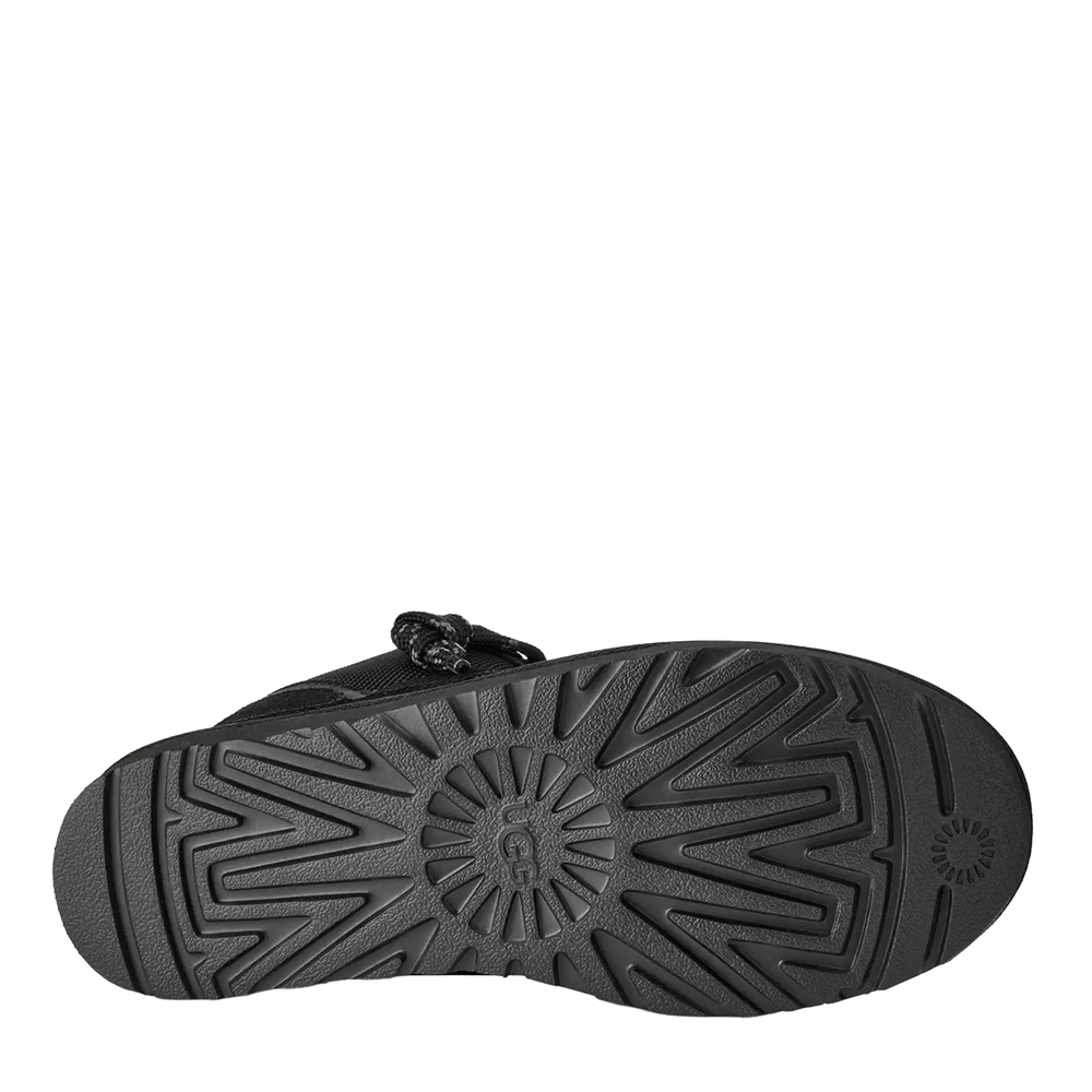 Bottom view of the black UGG low-top shoe, showcasing the solid black rubber outsole with a heavy circular lug pattern and the UGG logo molded into the center of the tread.