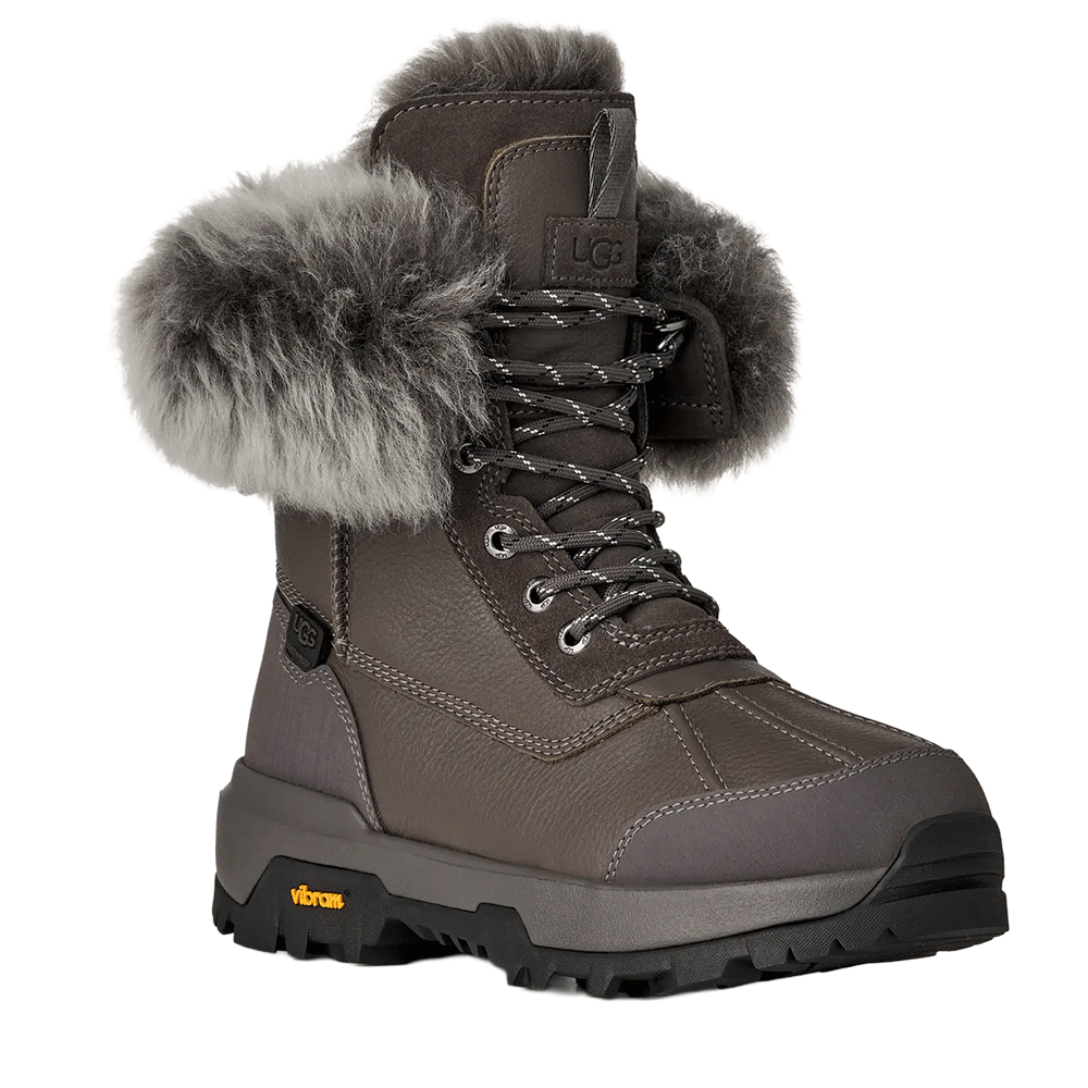 A pair of grey UGG women's winter boots with a thick, fluffy grey fur cuff and a heavy-duty black and grey Vibram sole.