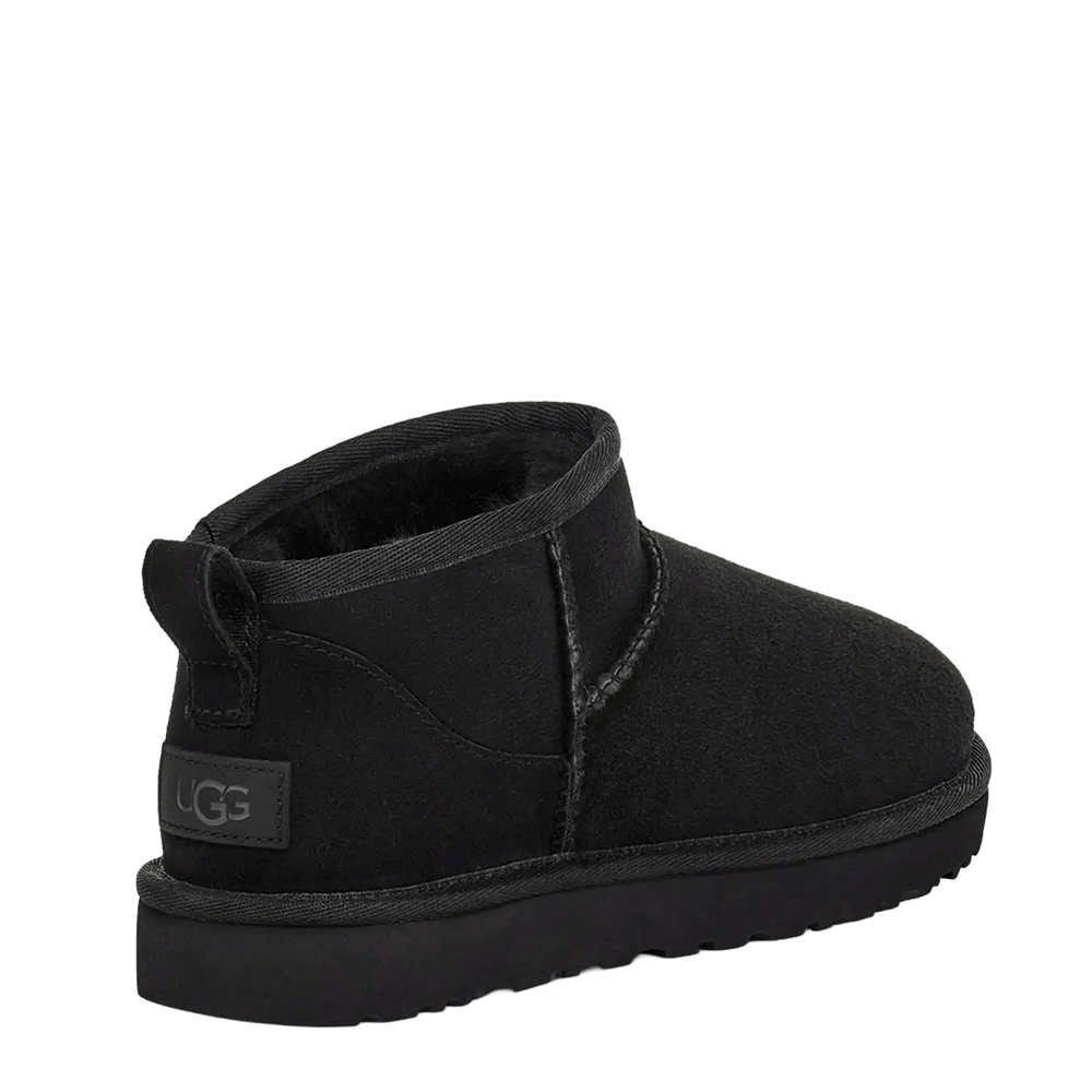 Rear view of a single UGG Women's Classic Ultra Mini boot in black. The image highlights the black UGG logo patch on the heel, the heel pull tab, and the dark sheepskin lining visible inside the extremely short shaft.