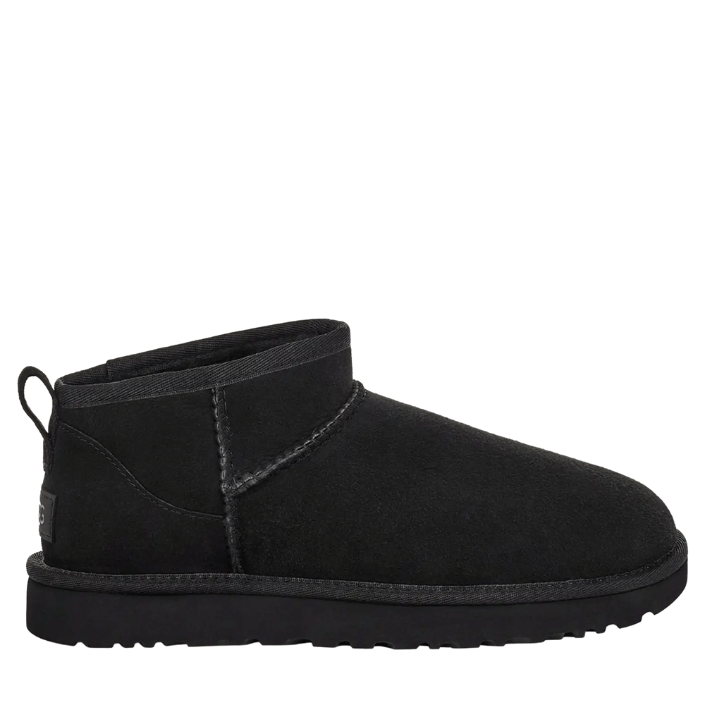 A side-view studio shot of a single UGG Women's Classic Ultra Mini boot in solid black. The boot features a very low ankle-cut shaft, black suede upper, gray stitching along the seams, and a black sole with subtle ridging.
