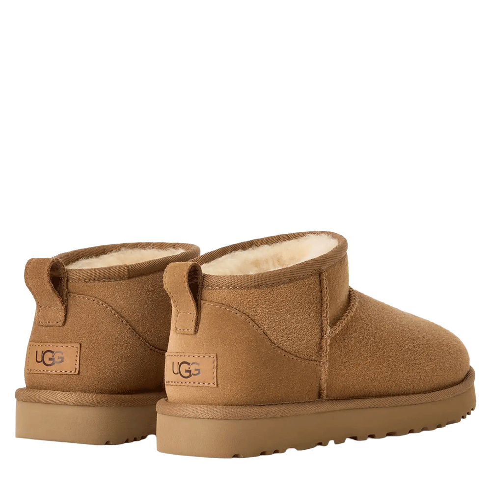 Rear view of a pair of UGG Women's Classic Ultra Mini boots in chestnut, angled slightly outward. The image highlights the UGG logo patch on the heel of both boots, the heel pull tabs, and the white sheepskin lining visible at the cuff.