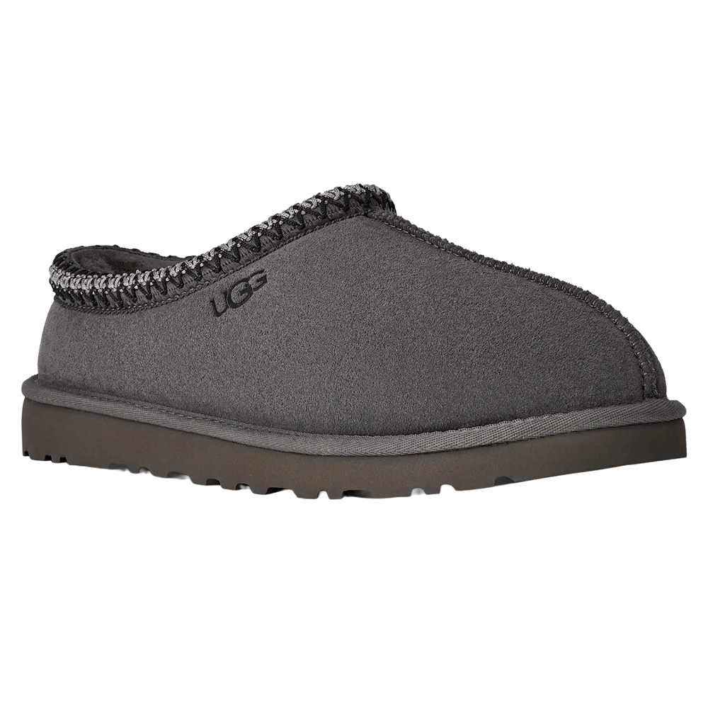 Angled view of the dark gray UGG Tasman II slipper. The slipper features a suede upper, dark gray Sugarcane EVA outsole, and the gray and white UGGbraid trim around the collar. The UGG logo is embossed near the trim.