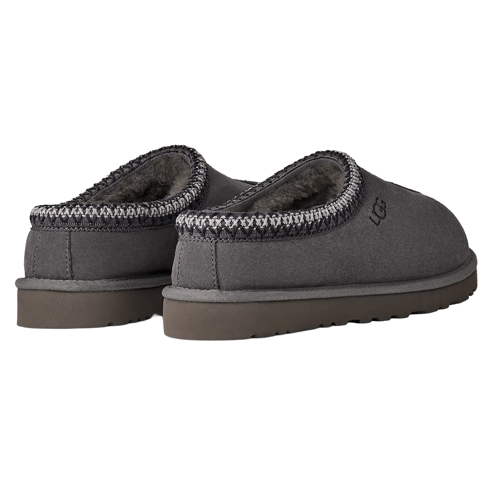 Rear-facing pair of dark gray UGG Tasman II slippers. The image shows the heel, the dark sheepskin lining visible at the collar, and the gray and white UGGbraid trim. Both slippers are set on a dark gray Sugarcane EVA outsole.