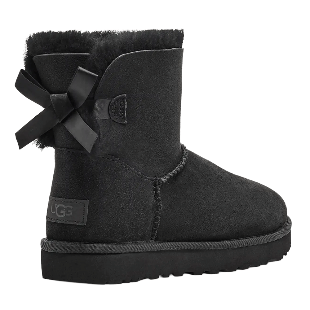 Side/rear view of the Black UGG Mini Bailey Bow II boot, showing the short Twinface sheepskin shaft, the plush black fur cuff, the fixed black satin bow at the heel, and the embossed UGG leather heel label.
