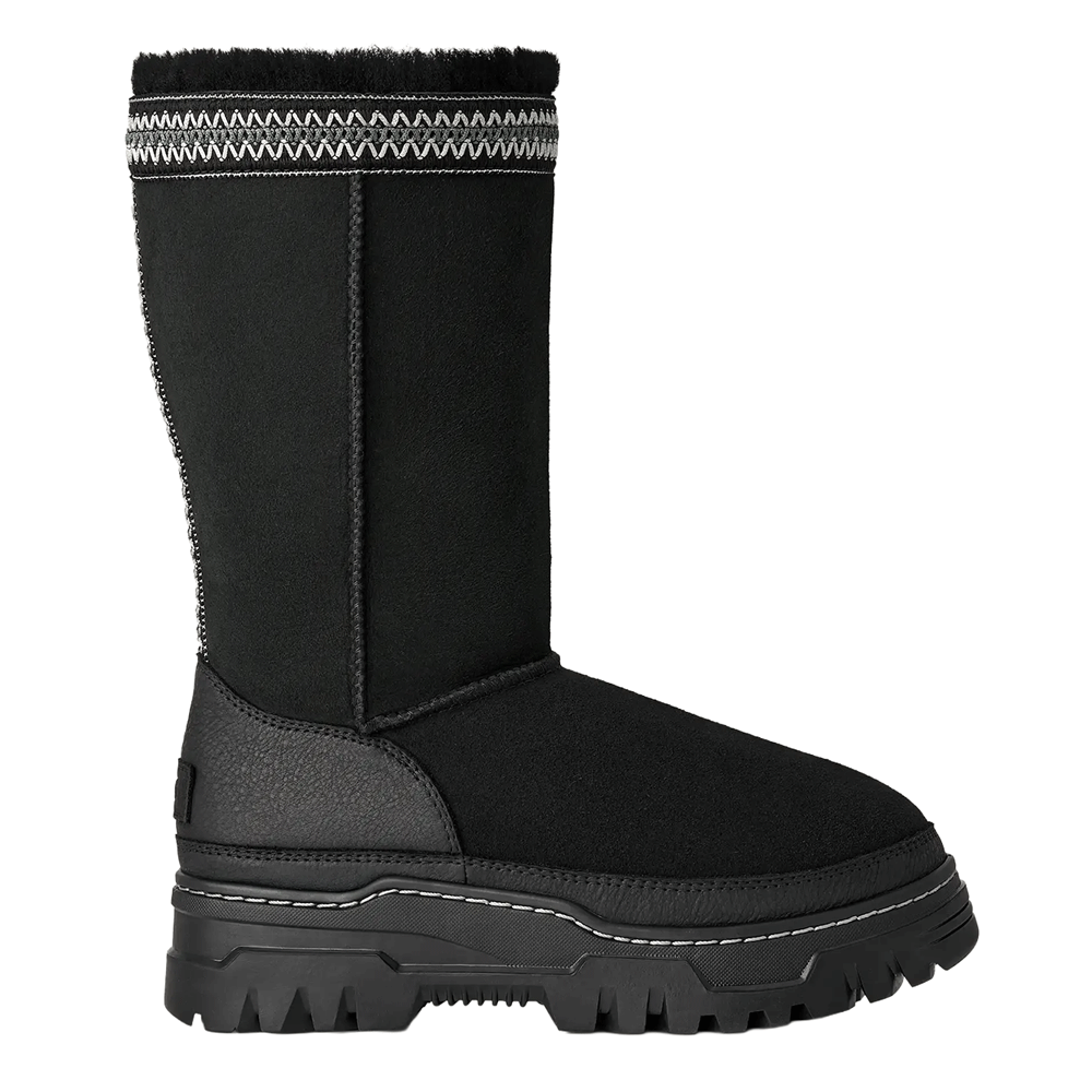 Side view of a tall, black UGG Classic Tall TrailGazer boot with a chunky black sole, a black leather mudguard, and a black and white decorative woven band at the cuff.