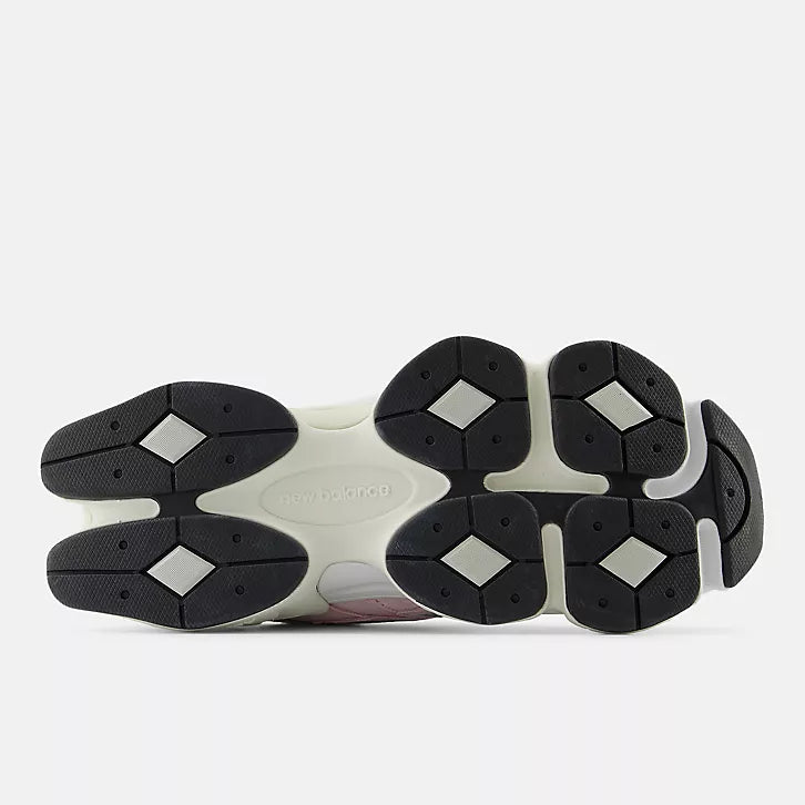 Bottom view of the New Balance 9060 sneaker outsole. The image shows the futuristic diamond-patterned traction pods in black and grey, the sculpted cream-colored midfoot with "New Balance" embossed in the center, and the wide, stable base design characteristic of the 9060 silhouette.