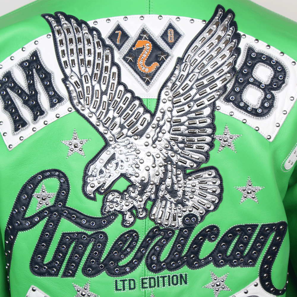 A close-up of the back of a green Pelle Pelle jacket featuring a large eagle with spread wings. The eagle is intricately detailed with silver metallic studs and sits above a script "American" patch. Below the script, a small "LTD EDITION" tag is embroidered in green. The design is flanked by large "M" and "B" block letters and small silver-studded stars.
