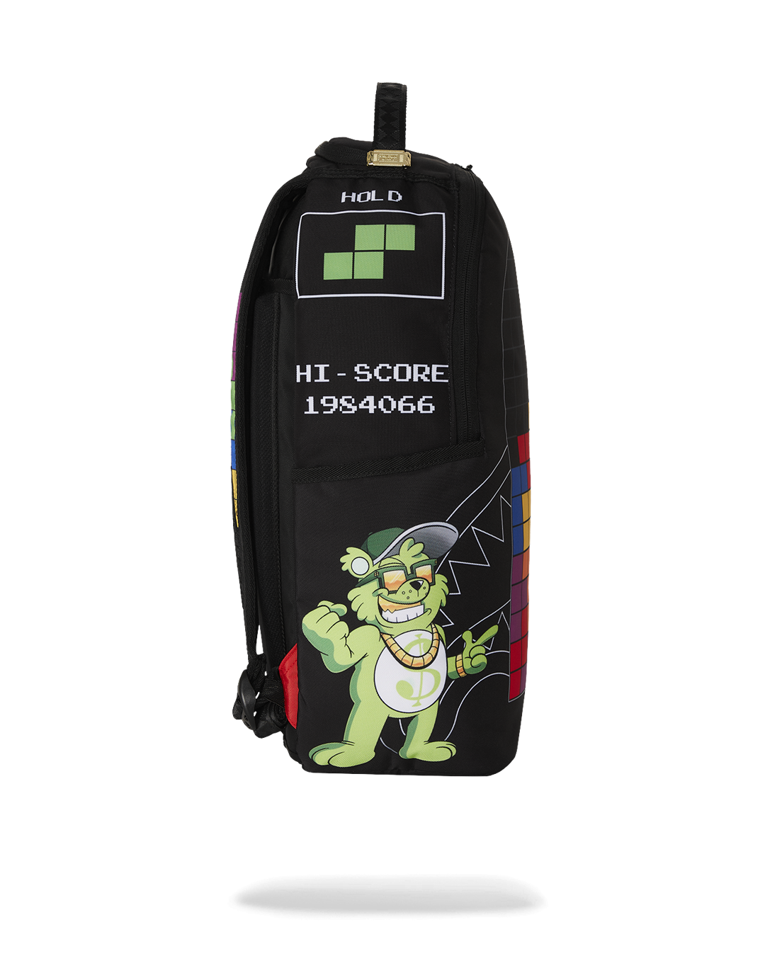 A black Sprayground backpack featuring a colorful Tetris design on the side. The main panel shows a grinning green monster with a backwards baseball cap and gold chain. Above the monster are white graphics that read "HOLD" with a green Tetris block and "HI-SCORE 1984066."
