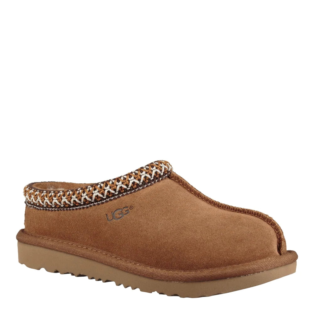 Angled view of a single UGG Kids Tasman slipper in chestnut, showing the soft suede upper and the braided trim around the collar. The low-profile sole has subtle ridging and the UGG logo is debossed on the side.