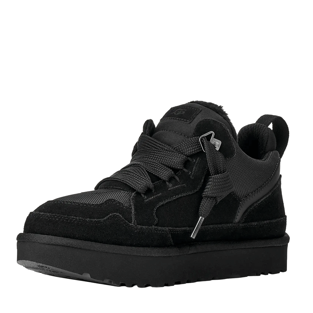 Front view of a black UGG low-top shoe, showcasing the black suede and mesh material combination, thick black laces tied in a bow, and the chunky black platform sole.
