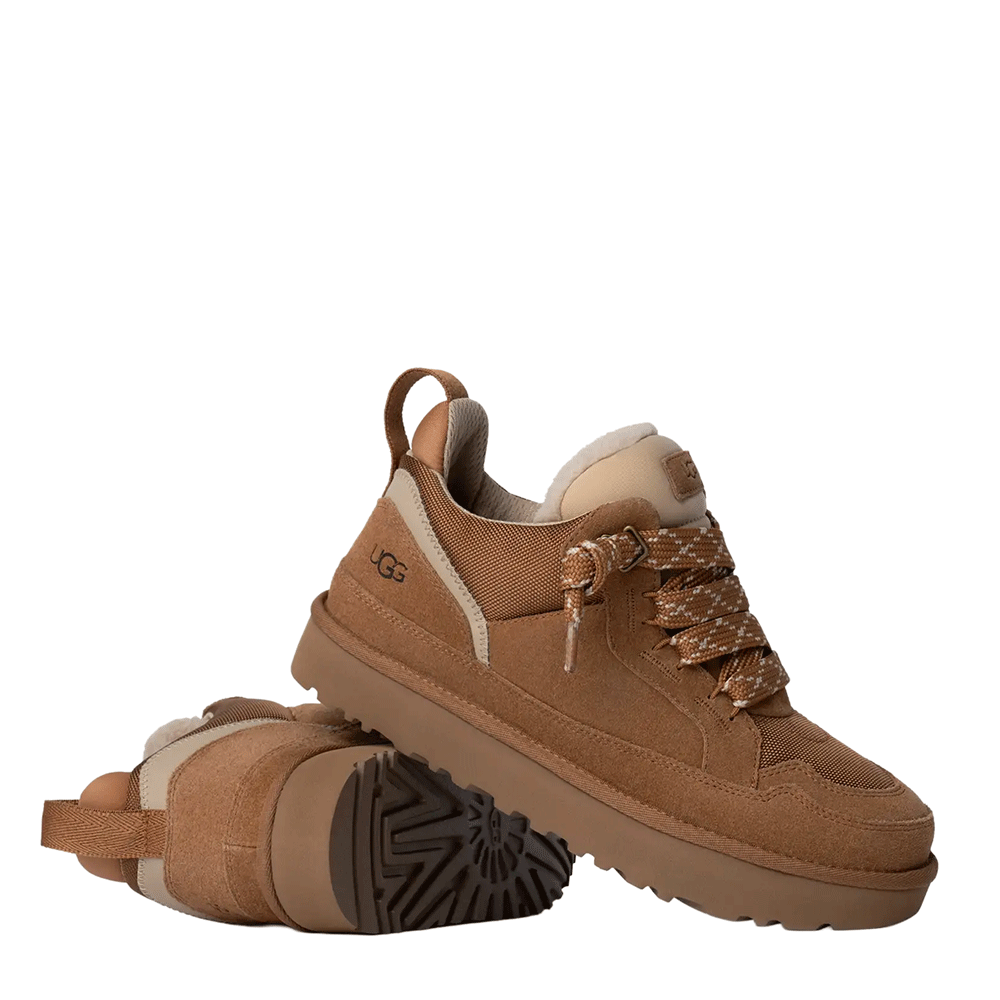 A pair of chestnut suede UGG low-top shoes, with one standing upright showcasing the textured upper and the other lying on its side to display the bottom of the brown lugged outsole.