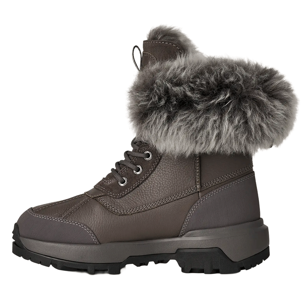 Side profile of a grey leather UGG winter boot, showcasing the textured leather body, lace-up front, durable grey sole, and thick grey fur lining the cuff.