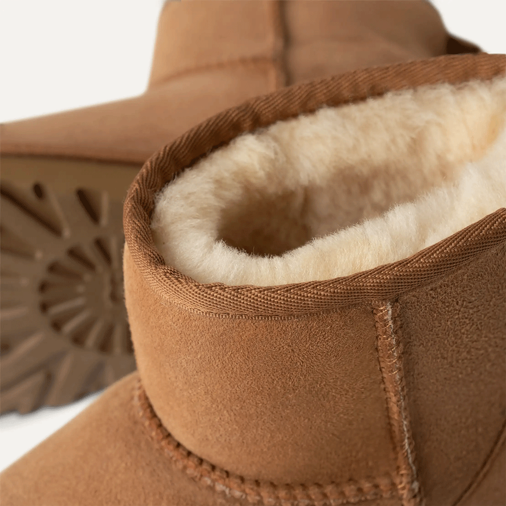 Close-up detail shot of the UGG Women's Classic Mini boot cuff in chestnut. The image clearly shows the thick, creamy-white sheepskin wool lining on the interior, the finished binding on the collar, and the deep tread of the outsole visible in the background.