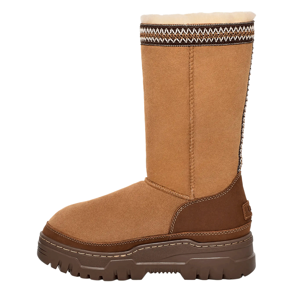 Side profile of the Chestnut UGG Classic Tall TrailGazer boot, showing the tall Twinface Sheepskin shaft, the decorative UGGbraid pattern at the cuff, and the contrast dark brown leather heel counter above the chunky platform sole.