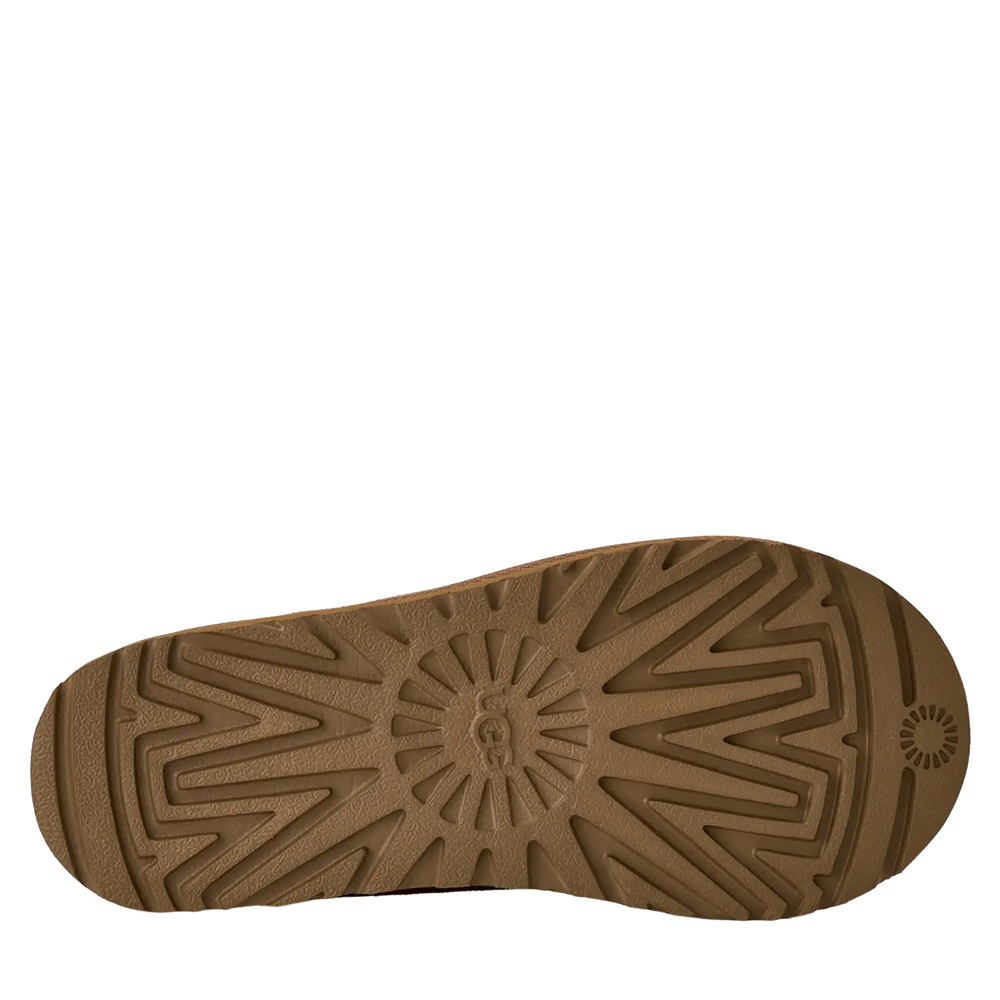 A view of the brown outsole of the UGG Tasman II slipper. The sole features a durable, textured tread pattern, including a large sunburst-like design and the UGG logo molded into the center of the heel area.