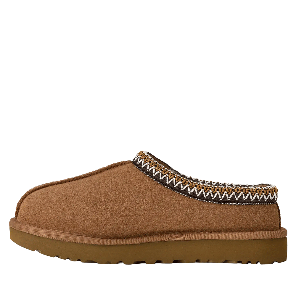 A side profile of a single UGG Tasman II slipper in a warm, chestnut-colored suede. The slipper has a sturdy brown outsole and the collar is trimmed with a distinctive, patterned UGGbraid, featuring zig-zag stitching in white and brown.