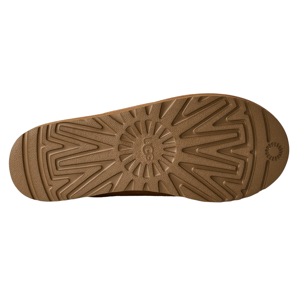 Bottom view of the UGG Tasman II slipper's outsole. The image shows the full length of the tan/brown Sugarcane EVA outsole, featuring a deep, ridged traction pattern centered around a circular UGG logo detail.