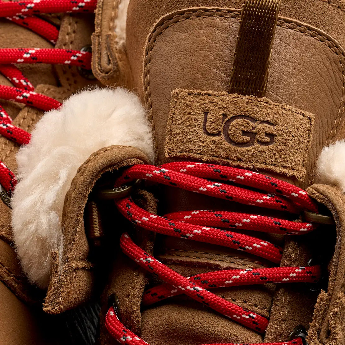 Close-up of a UGG boot with red laces and white fur lining.