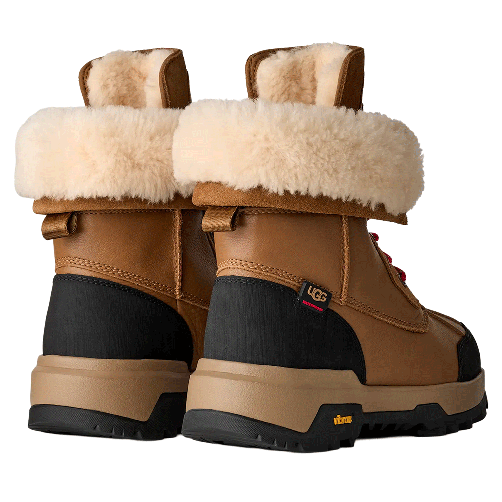 Rear view of a pair of Chestnut UGG Adirondack Boot XXV winter boots, showing the cuffable shaft with a cream-colored fur lining, black leather accents, and the rugged black and beige Vibram outsole.