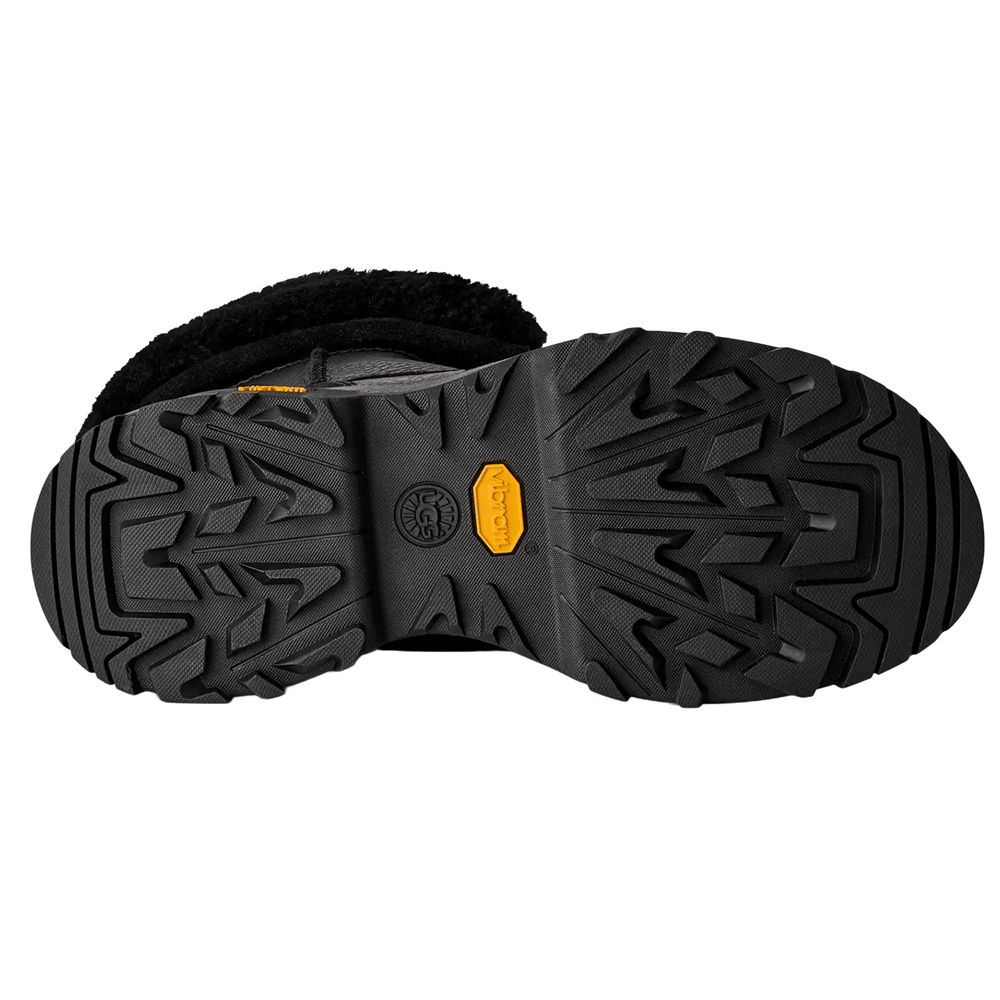 Bottom view of the Black UGG Adirondack Boot XXV, showcasing the heavy-duty black Vibram outsole with aggressive multi-directional treads and a prominent yellow Vibram logo.