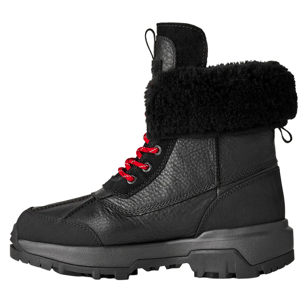 Side view of the Black UGG Adirondack Boot XXV, featuring a waterproof leather upper, a fluffy black fur cuff, a lace-up front with striking red laces, and a rugged black Vibram outsole.