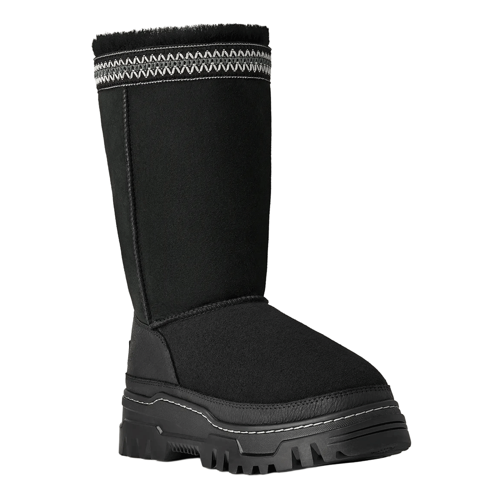 Front view of the tall, black UGG Classic Tall TrailGazer boot with a chunky black sole, a black leather mudguard, and a black and white decorative woven band at the cuff.