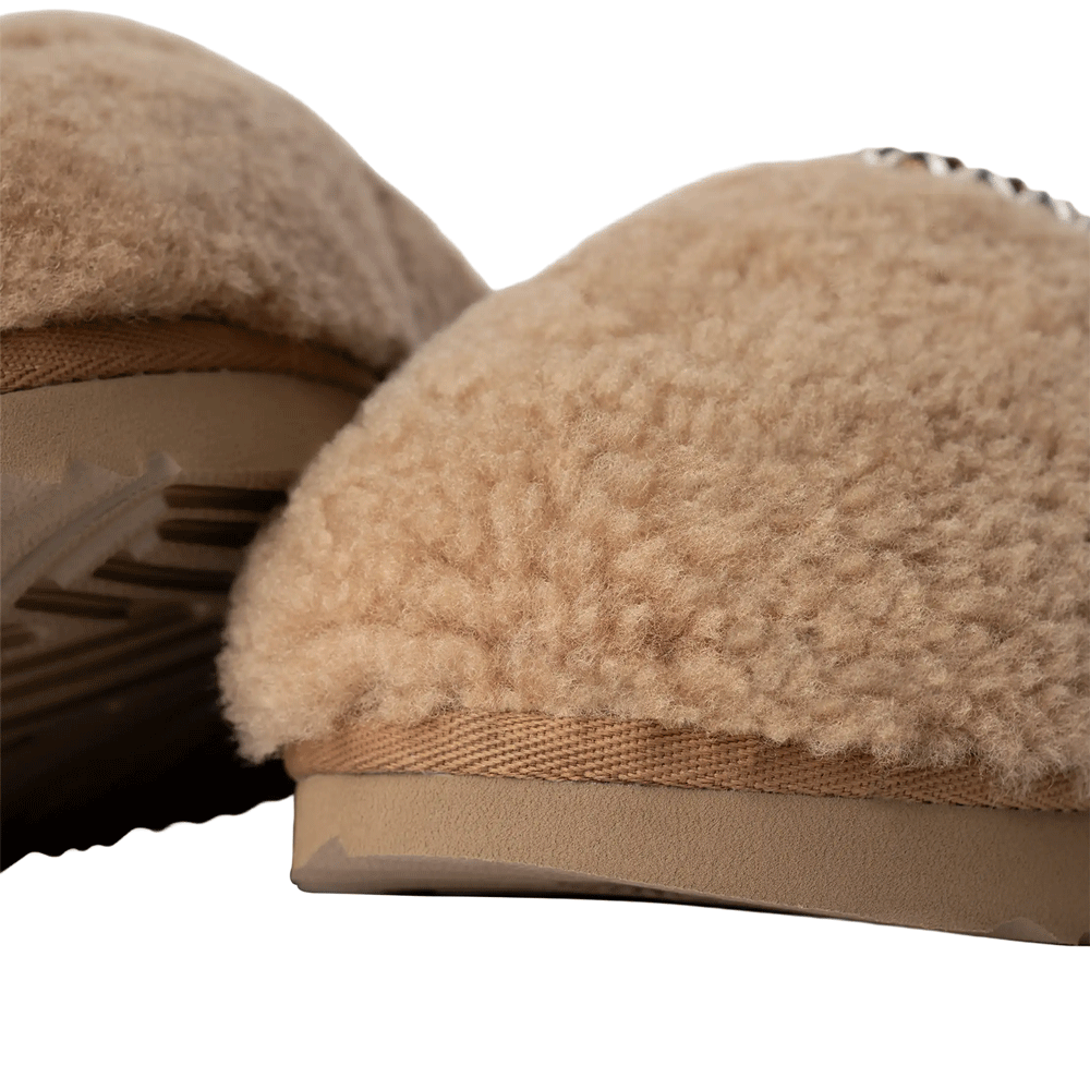 Extreme close-up of the Chestnut Tasman Maxi Curly slipper's heel and outsole, showing the dense, curly sheepskin texture and the textile binding above the ridged platform sole.