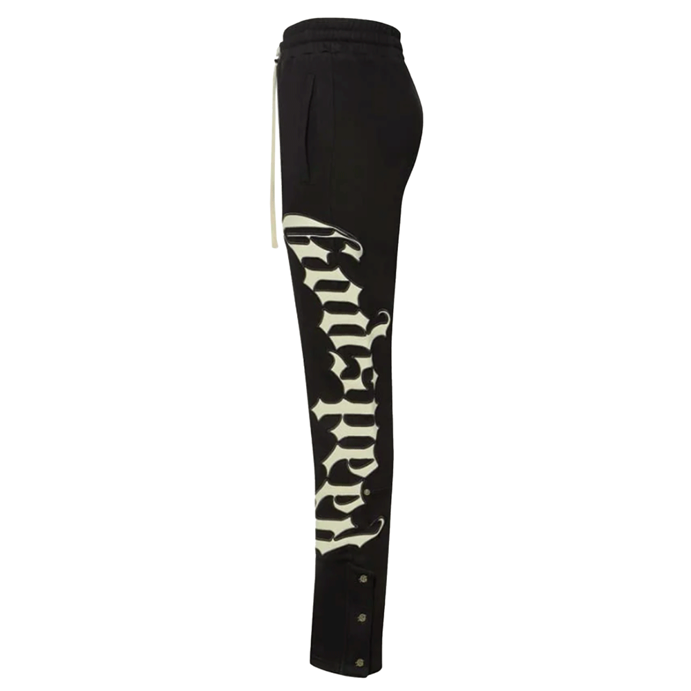 Side view of Godspeed OG Logo V2 black sweatpants highlighting the large, vertical white Gothic "Godspeed" logo running down the entire length of the left leg. The image also shows the long cream drawstring at the waist and the silver snap-button detailing at the outer ankle.