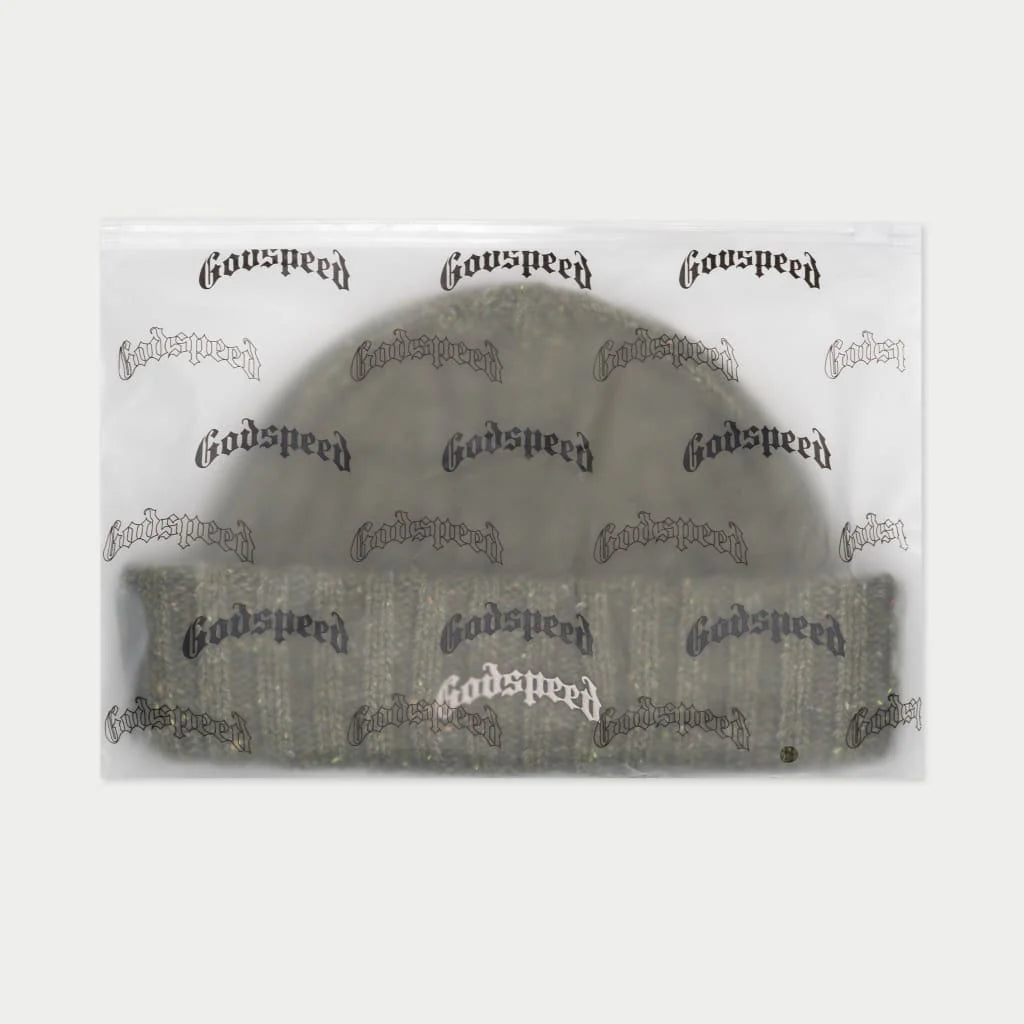 A "Godspeed" beanie in a comfortable olive green with multicolored speckles, packaged in a clear plastic bag with the brand logo repeated across it. The stylish and new beanie is ready for delivery.