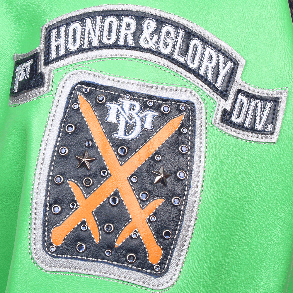 Close-up of the "Honor & Glory Div." sleeve patch on a green Pelle Pelle leather jacket. The design features an arched black and silver banner over a black leather shield with orange crossed swords, metallic silver studs, and a central embroidered "MB" logo.