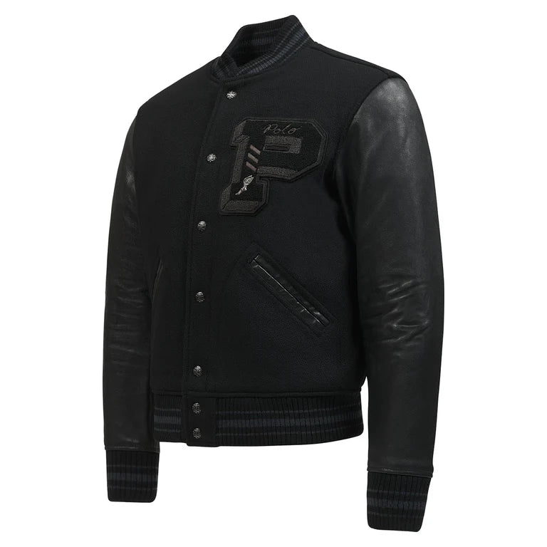 A three-quarter view of the all-black Polo Ralph Lauren Iconic Letterman Jacket. The image highlights the contrast between the matte melton wool body and the smooth leather sleeves, the large chenille "P" patch on the chest, and the athletic, striped ribbing on the cuffs and hem.